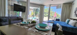 Une chambre d’hôtel moderne dotée d’un coin repas, d’un canapé, d’un téléviseur fixé au mur et d’un balcon offrant une vue sur l’extérieur.