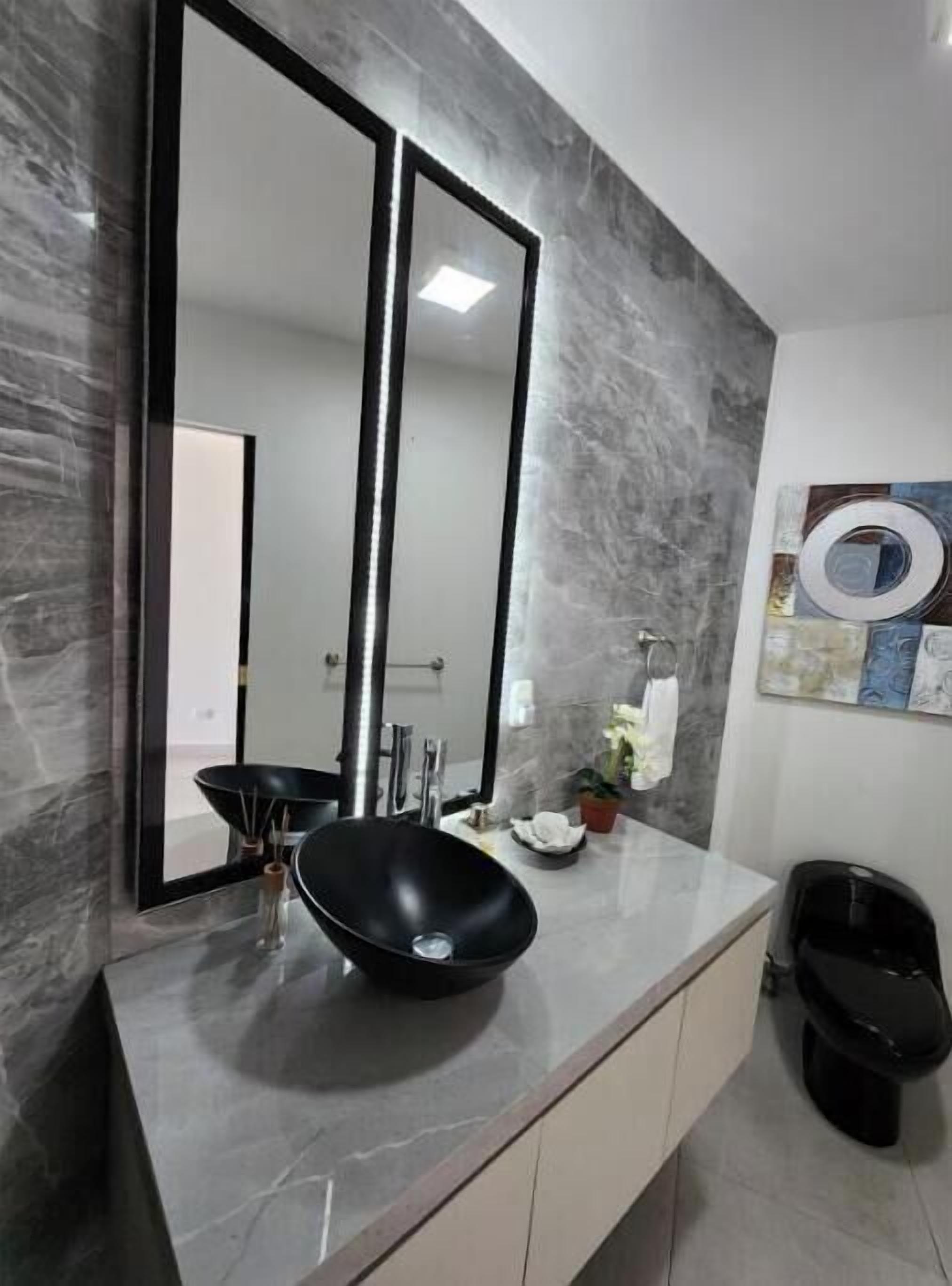 A modern bathroom with a black sink, two mirrors, a toilet, and a marble wall.