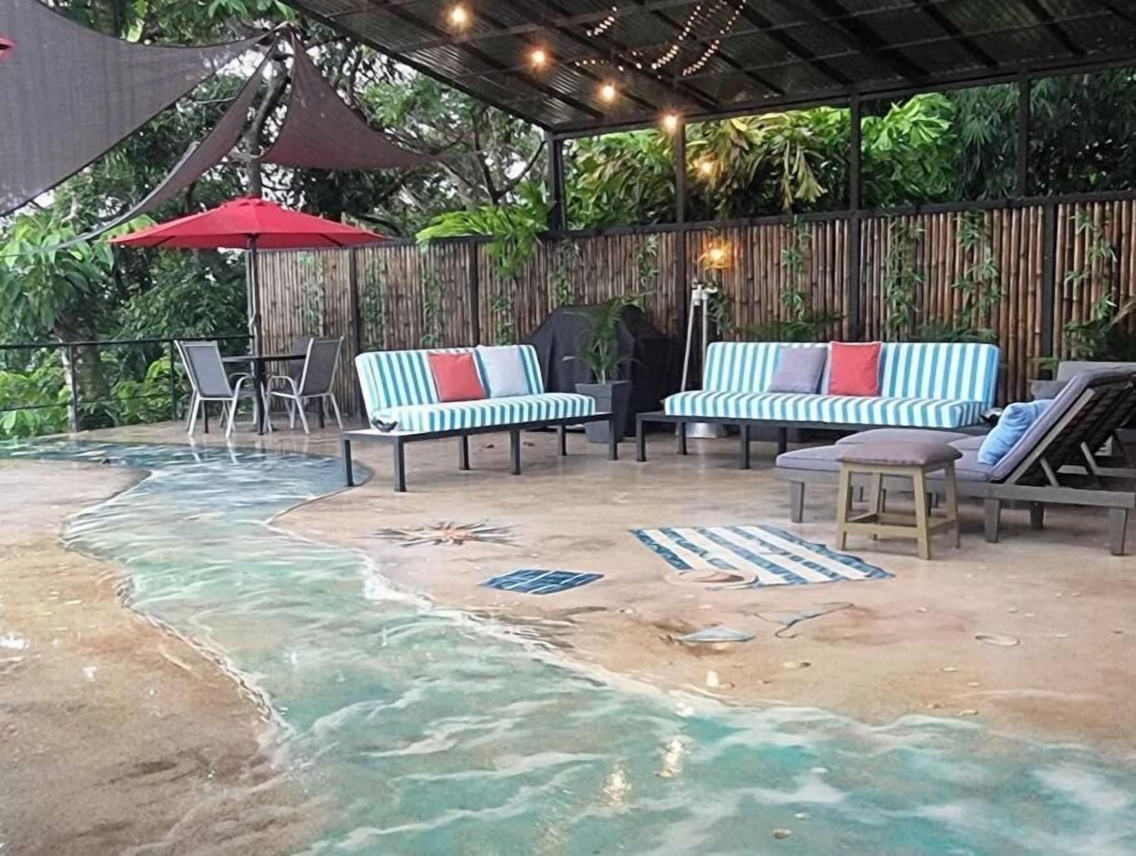 A covered outdoor area with a pool, lounge chairs, and a red umbrella.