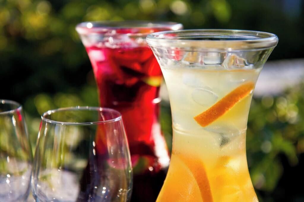 Three glasses of beverages with an orange slice, one in a clear glass and two in red glasses.