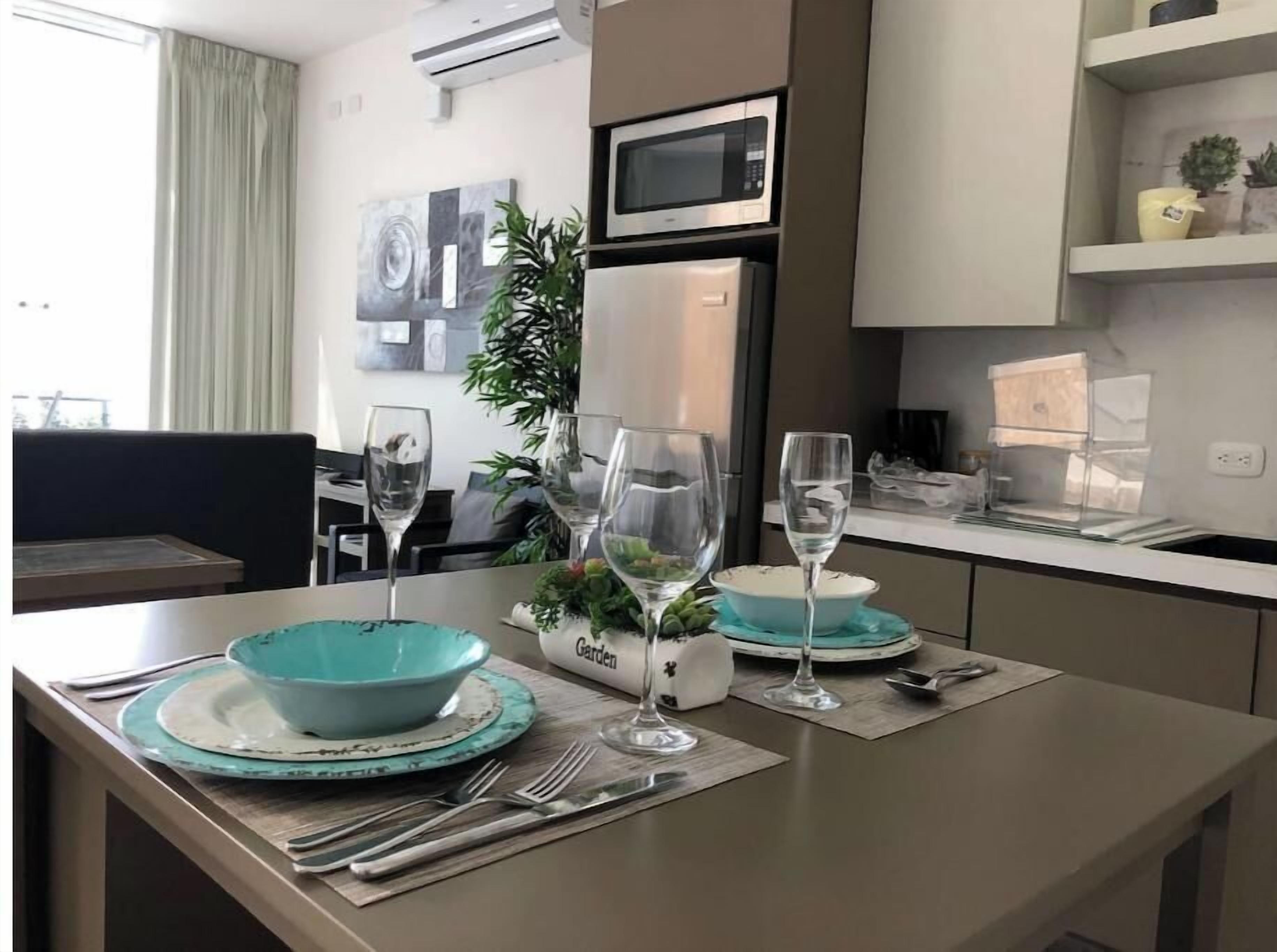 A modern kitchen with a dining area. It includes a microwave, refrigerator, and a dining table set with plates, glasses, and cutlery.