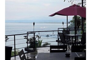 Un espace extérieur aménagé avec des tables et des chaises, offrant une vue sur la mer, et agrémenté d'un parasol rose.