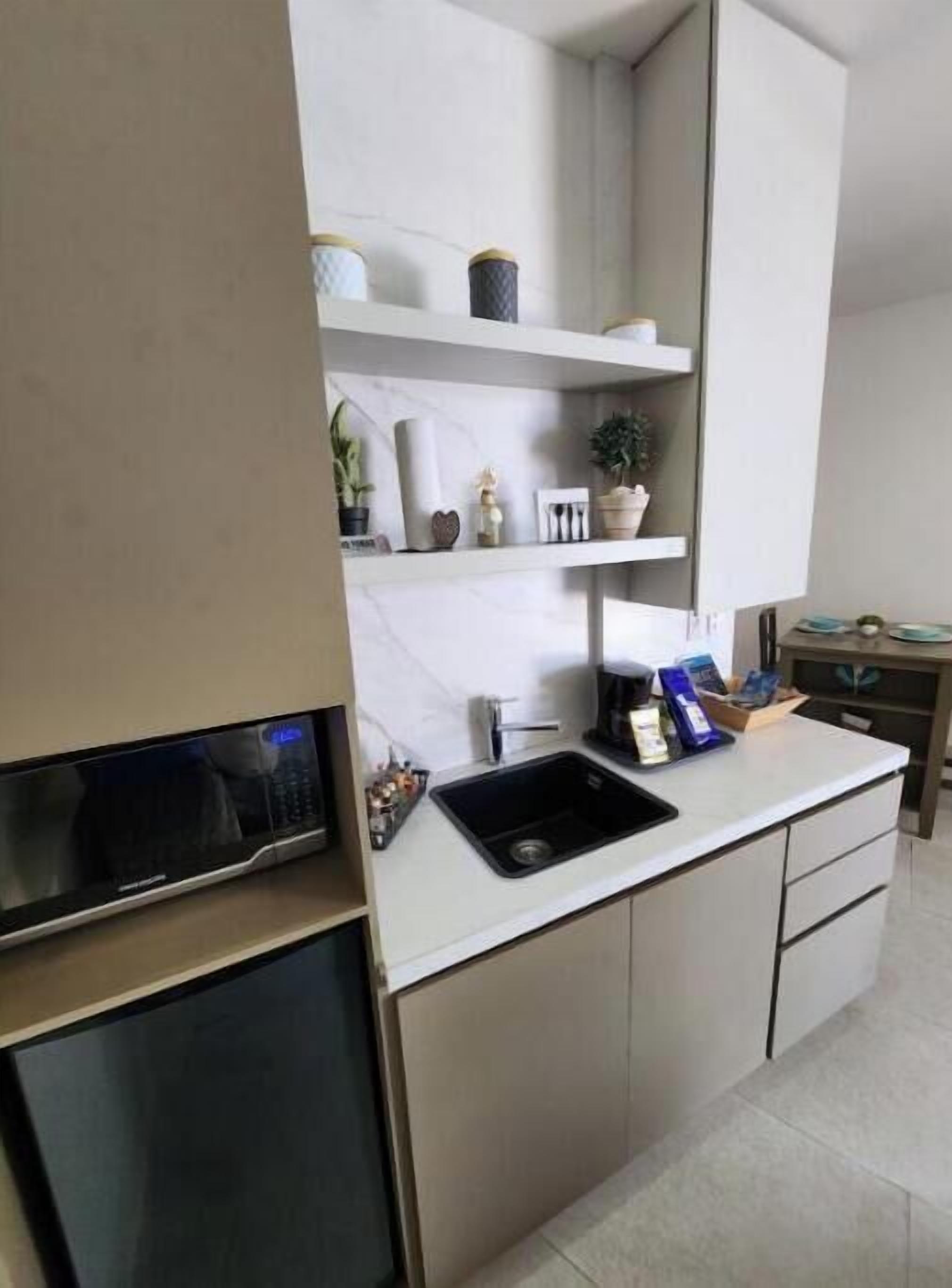 A modern kitchen with a built-in microwave, a sink, and a coffee maker. There are shelves with decorative items and a small plant.