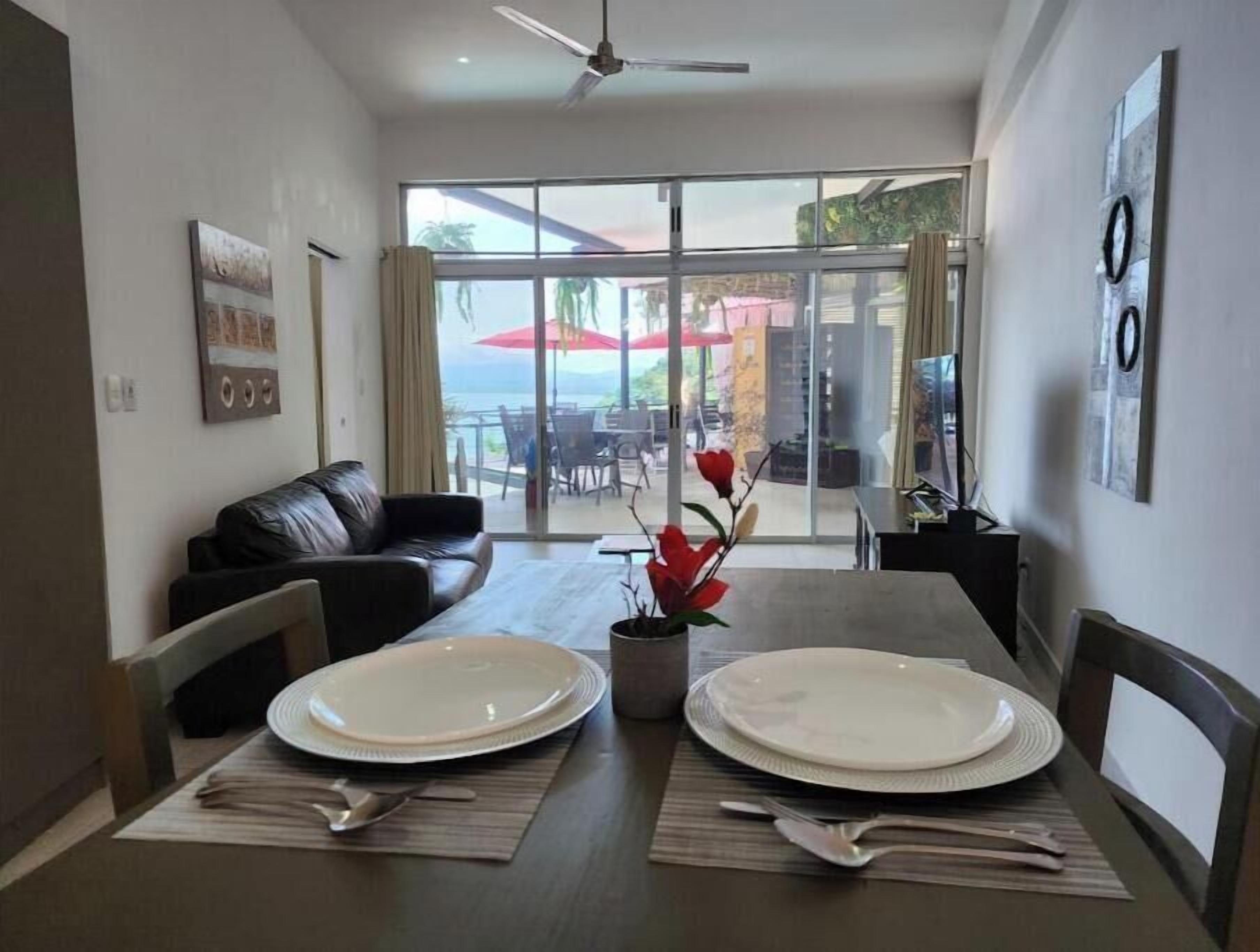 A dining area with a table set for two, a sofa, and a view of the outdoors.