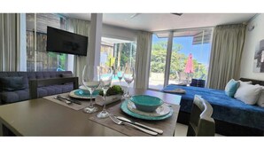 A modern hotel room with a dining area, a sofa, a TV mounted on the wall, and a balcony with a view of the outdoors. - Suite 7 Hotel VOS - Superior Suite, Ocean View (Manuel Antonio)