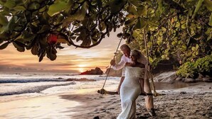 A beach scene with a couple under a tree, a sunset in the background, and the ocean. - Suite 7 Hotel VOS - Superior Suite, Ocean View (Manuel Antonio)