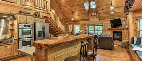 A spacious log cabin interior with a kitchen, dining area, and a fireplace.