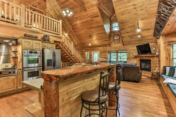 A spacious log cabin interior with a kitchen, dining area, and a fireplace.