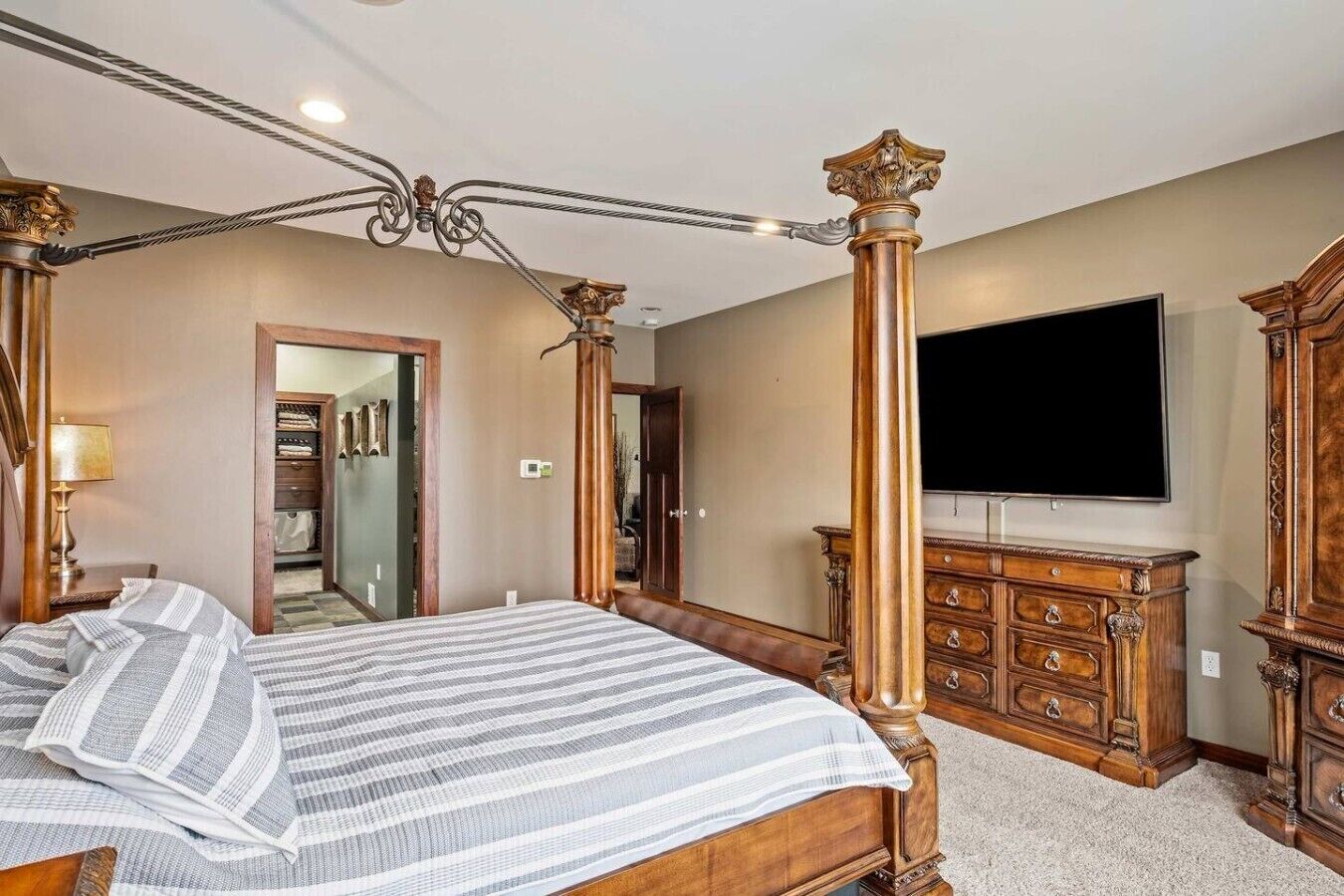 Un dormitorio con cama con dosel, televisor, cómoda de madera y vestidor.