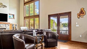 Un salon comprenant un canapé d’angle, des fauteuils en cuir, un téléviseur à écran plat et une cheminée en pierre.