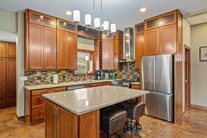 A kitchen with wooden cabinets, a stainless steel refrigerator, a central island with bar stools, and a tiled backsplash.