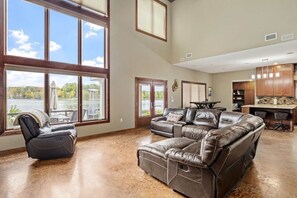 A spacious living room with a large leather sectional sofa, a recliner, and a view of a lake through large windows.