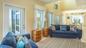A spacious living room with a blue sofa, wicker side tables, and a view of the sea through large windows.
