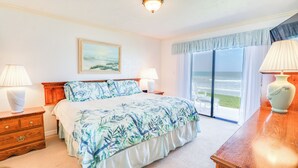 Ein Schlafzimmer mit Bett, Nachttischen, einem Schminktisch und einem Bild, mit Blick auf das Meer.