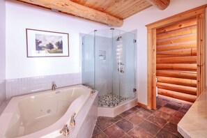 Un baño con una bañera grande, ducha con mampara de vidrio y puerta de madera.