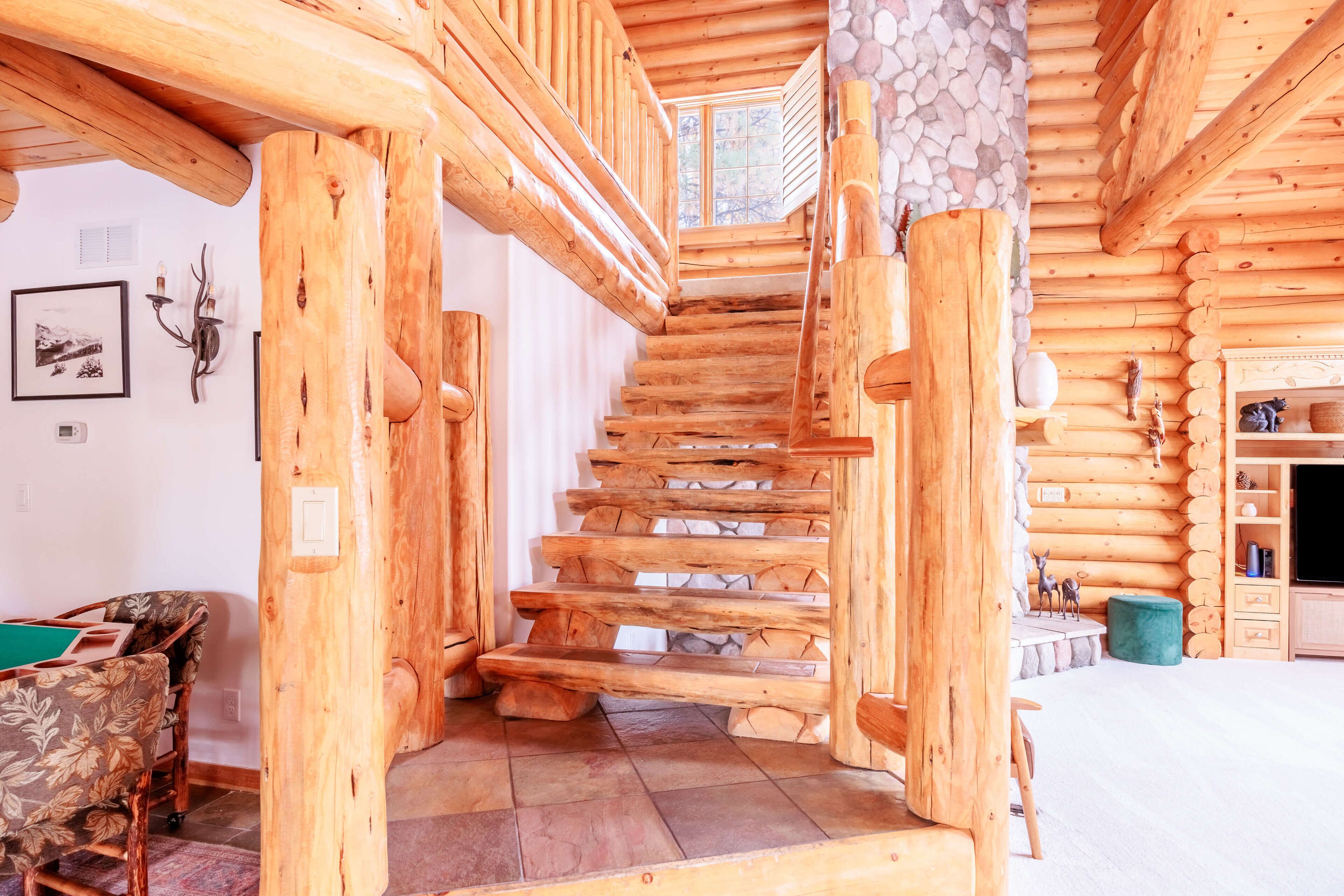 Ein Holzblockhaus-Innenraum mit einer Holztreppe, rustikalem Dekor und einem Kamin aus Stein.