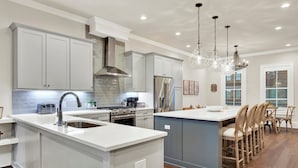 A modern kitchen with white cabinetry, stainless steel appliances, and a central island with bar stools.