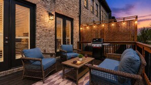An outdoor patio with wicker furniture, a grill, and a brick building.