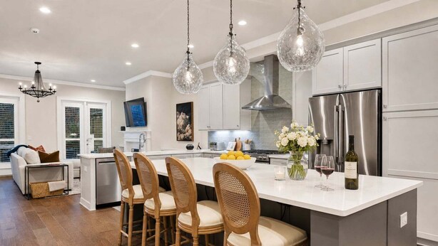 A modern kitchen with a central island, bar stools, pendant lighting, and stainless steel appliances.