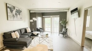 A modern living room with a dining area set for a meal, a black sofa, a white dining table, and a large window. - Stylish Black-themed Apartment in Des Moines (Des Moines)