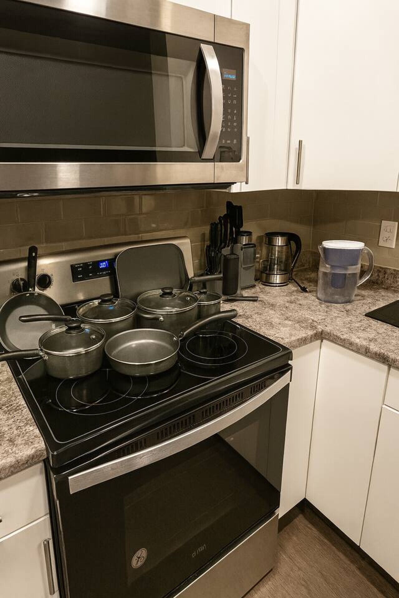 A kitchen with a microwave, stove, pots, and a coffee maker.