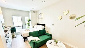 A modern apartment with a green sofa, a round coffee table, a bed with white bedding, and a small kitchen area. - Spacious Studio Unit in Des Moines (Des Moines)