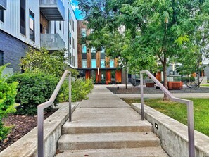 A concrete staircase leading to a building with a modern design, surrounded by greenery and outdoor seating.
