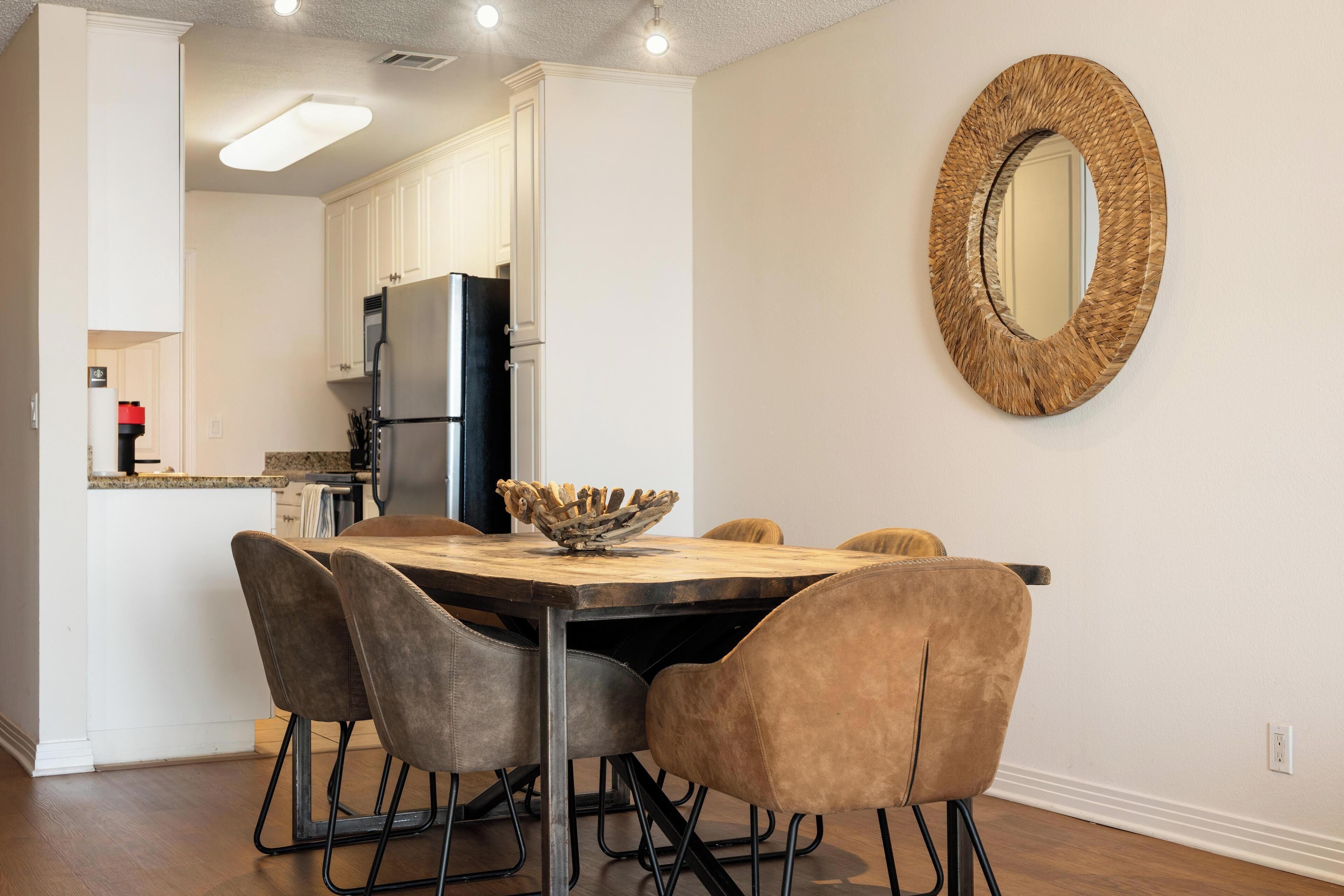 Un coin repas avec une table en bois, quatre chaises et un miroir décoratif au mur.