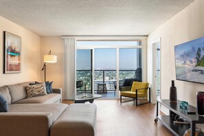 Una sala de estar moderna con un sofá, un sillón y una mesa. Un ventanal ofrece vistas de la ciudad.