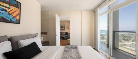 A bedroom with a large bed, a view of the city through the window, and a painting on the wall.