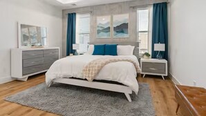 Une chambre à coucher avec un lit, des tables de chevet, une commode et une fenêtre avec des rideaux.