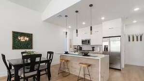 Une cuisine moderne avec des armoires blanches, un réfrigérateur en acier inoxydable et des luminaires suspendus.