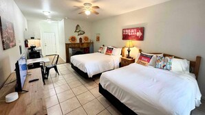 A hotel room with two beds, a desk, a ceiling fan, and a kitchenette. - Wasser Lodge #206 | Sleeps 4 | Comal Riverfront (New Braunfels)
