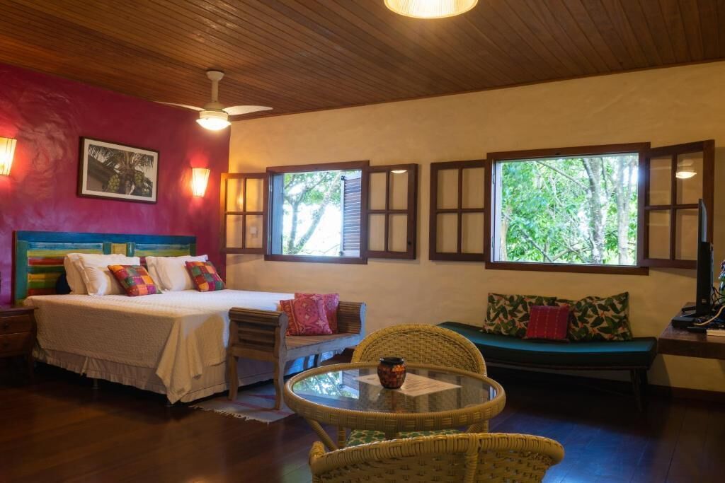 A room with a bed, a sofa, a table, and windows with shutters.