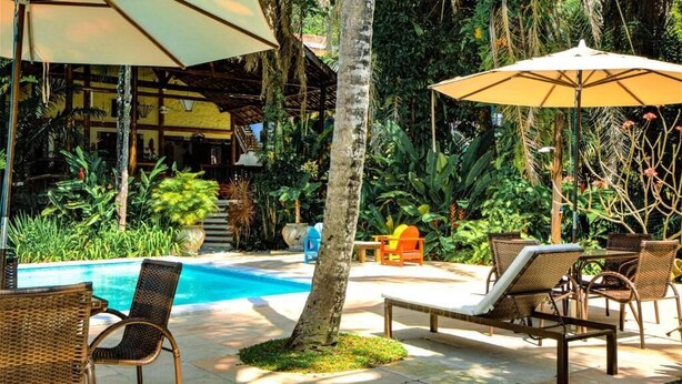 Zona de piscina con sillones de descanso, sombrillas y una pileta.