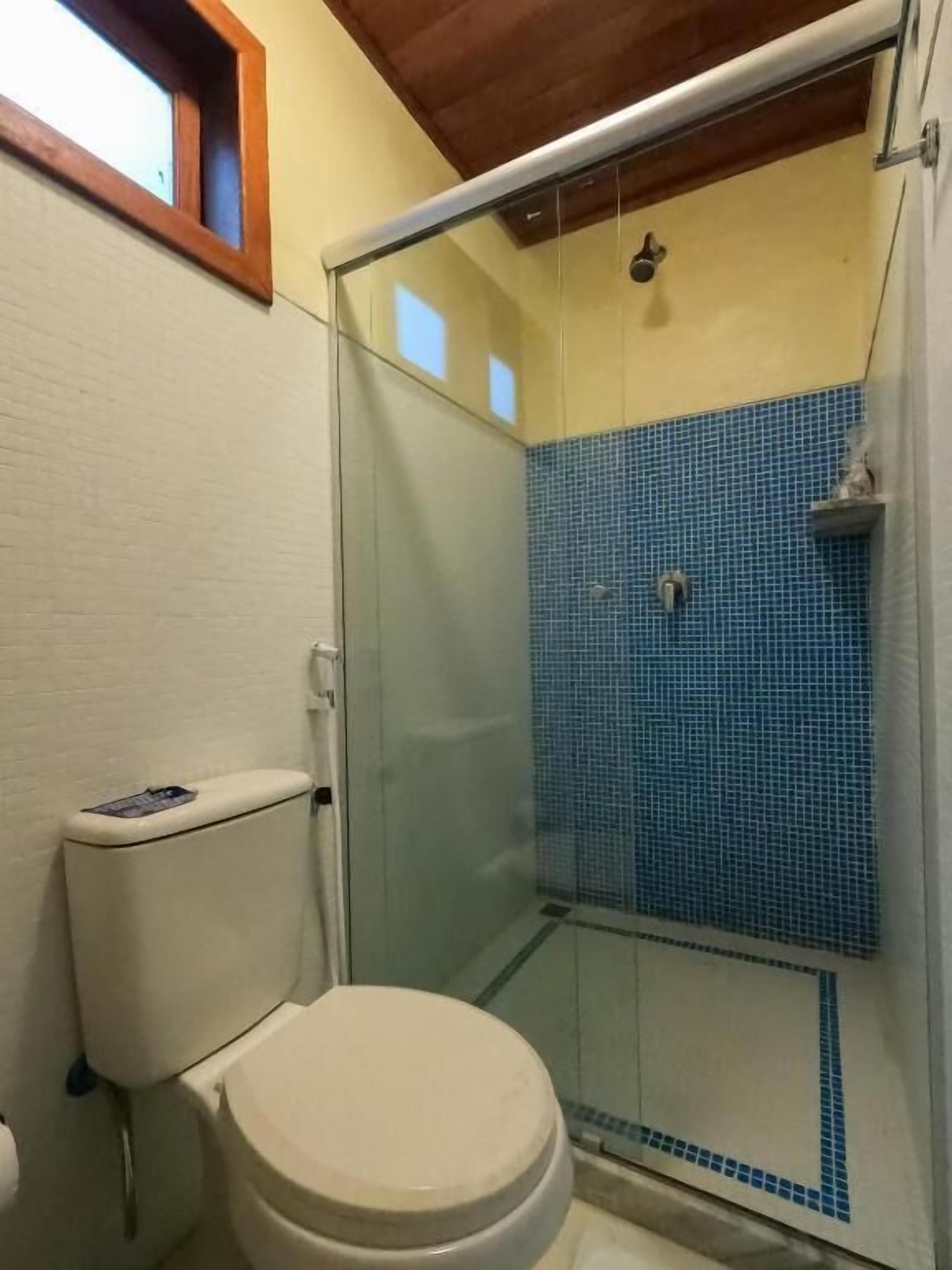 A bathroom with a toilet, a glass-enclosed shower with blue tiles, and a wooden ceiling.