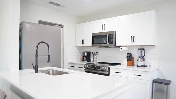 A modern kitchen with white cabinetry, a stainless steel sink, a built-in microwave, and a coffee maker.