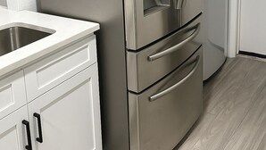A stainless steel refrigerator in a kitchen with white cabinetry and a wooden floor.