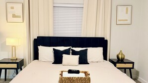 A neatly made bed with a headboard, two bedside tables with lamps, a ceiling fan, and a window with curtains.