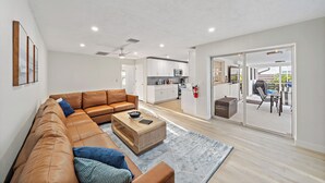 A modern living room with a leather sofa, a wooden coffee table, and a kitchen in the background.