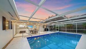 An indoor swimming pool with a glass ceiling, a seating area, and a view of the sky.