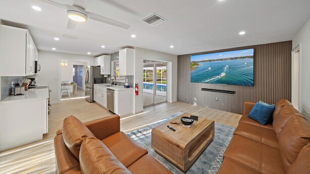 A modern living room with a large TV, leather sofas, a wooden coffee table, and a view of a swimming pool through the glass doors.