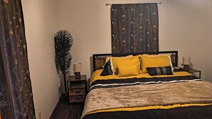 Un dormitori amb llit, taules de nit, una làmpada, una planta i cortines.