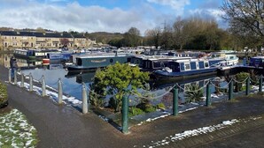 A canal with several narrowboats docked, surrounded by buildings and greenery.