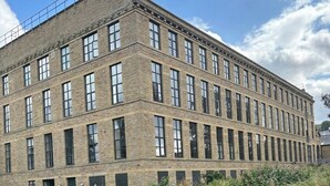 A multi-story brick building with large windows, situated next to a calm water body.