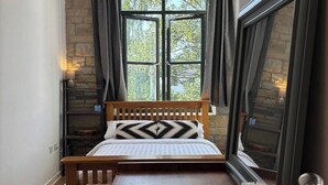A bedroom with a wooden bed, a large window with curtains, a chandelier, and a mirror.