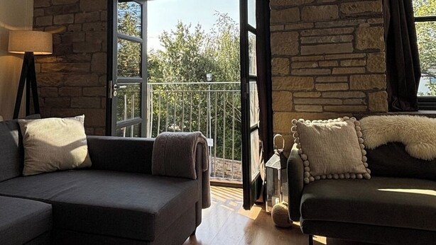A spacious living room with a stone wall, large windows, and a balcony.