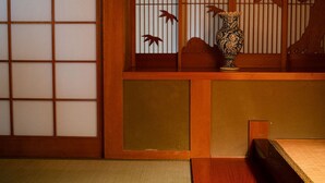 Una stanza tradizionale giapponese con pavimento in tatami, un paravento shoji con un motivo di gru e un vaso decorativo su una bassa mensola di legno.