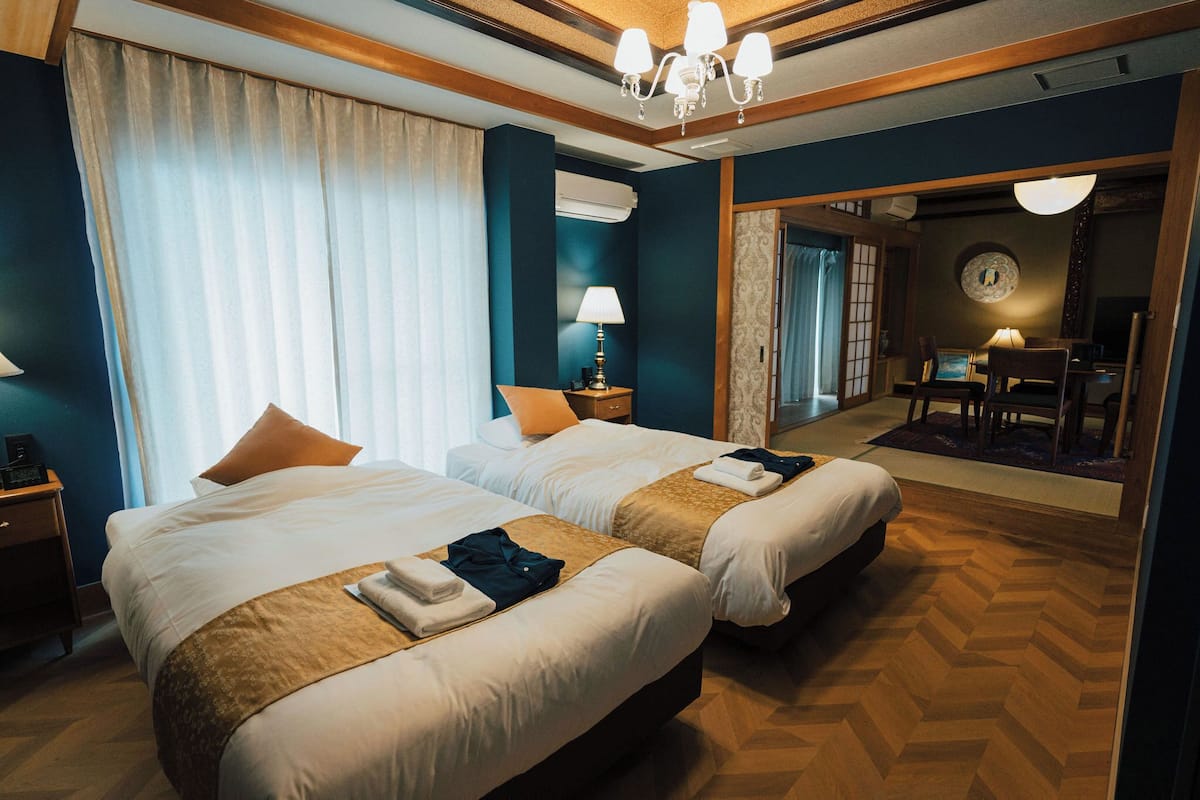A hotel room with two beds, a chandelier, a desk, and a mirror.