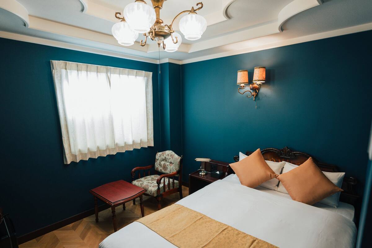 A hotel room with a large bed, a chair, a desk, and a chandelier.